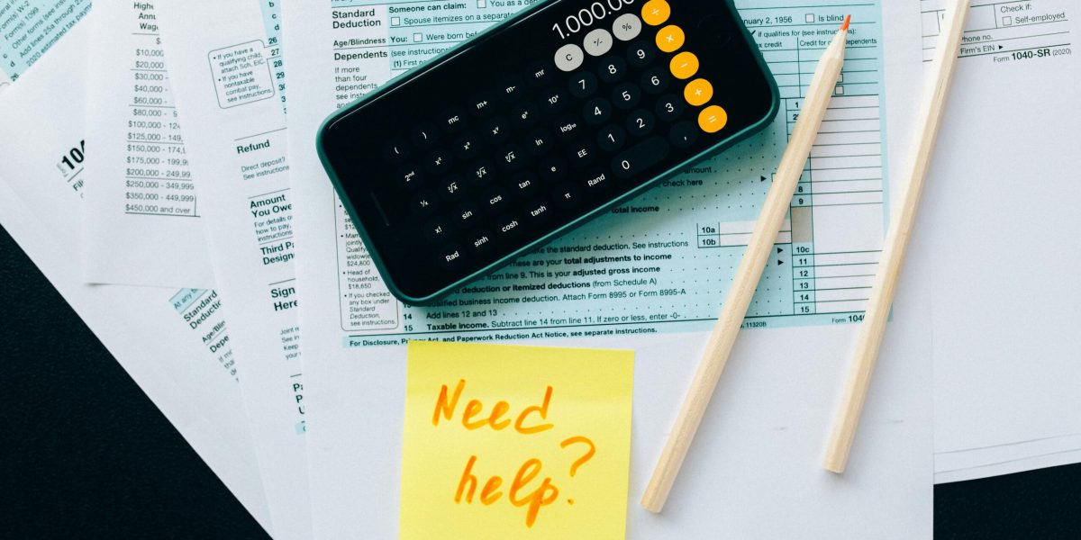 Top view of financial papers with a calculator, pencils, and a note saying 'Need help?' indicating tax or accounting assistance.